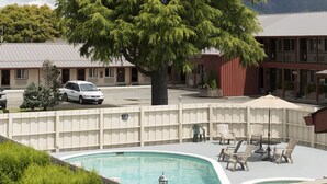 A pool area with lounge chairs and umbrellas, surrounded by a fence and a large tree. - The Forks Motel (Forks)