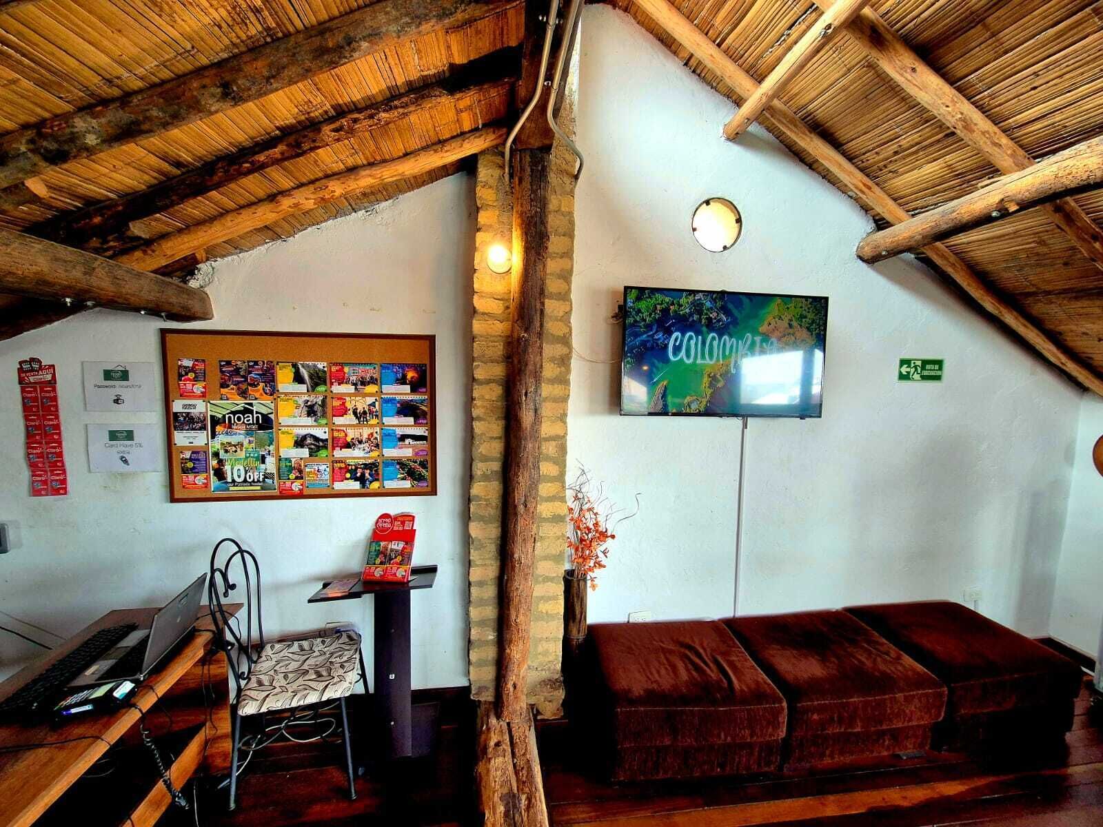 A cozy room with a wooden ceiling, a bulletin board with various notices, a flat-screen TV, and a comfortable sofa.