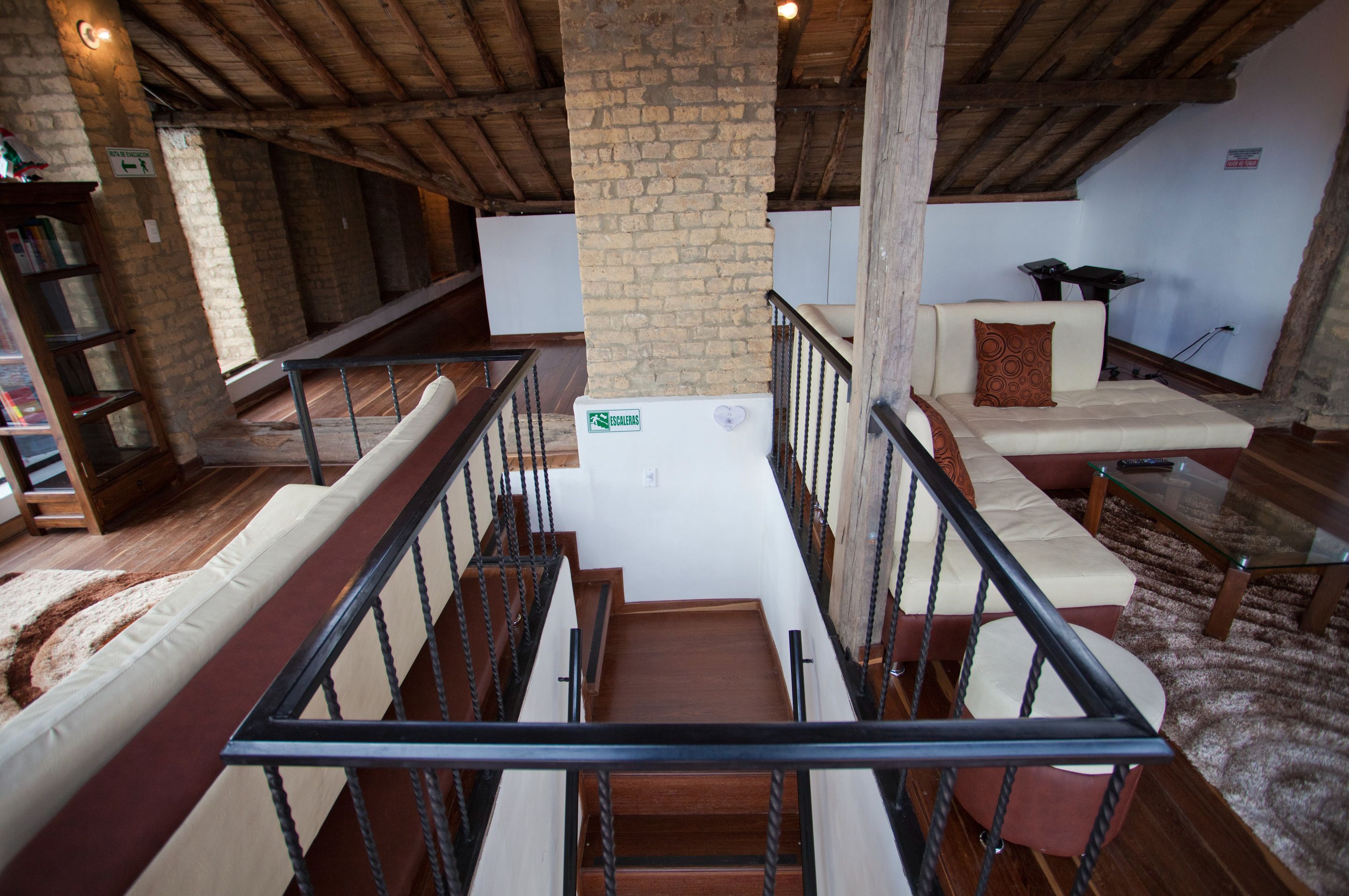 Ein geräumiger Loft mit hoher Decke, freiliegenden Backsteinwänden, einer Holztreppe und einer gemütlichen Sitzecke mit Sofa und Kissen.