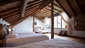 Une chambre avec deux lits, des poutres apparentes, une fenêtre avec des rideaux, une table de chevet et un extincteur fixé au mur.