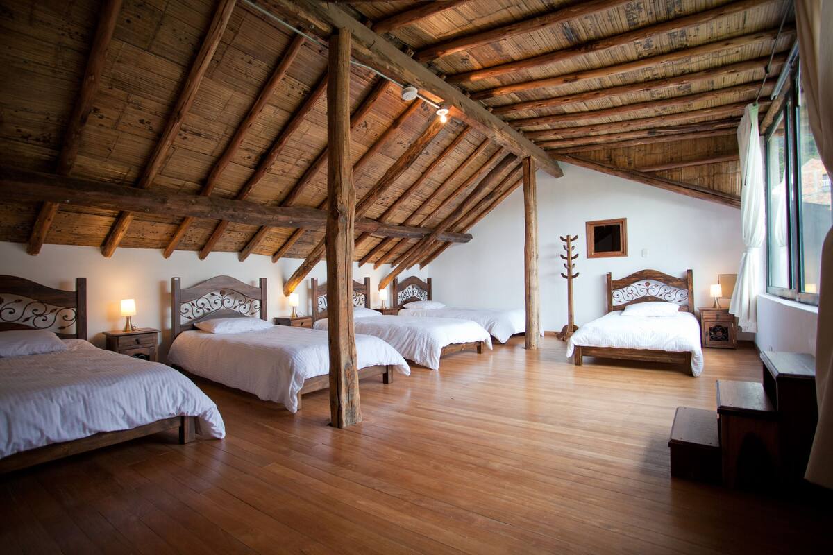 A spacious room with wooden floors and a sloped ceiling, featuring four beds arranged in a row.