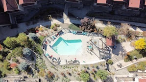 Vista aérea de un patio con piscina, rodeado de árboles y edificios con tejados rojos.