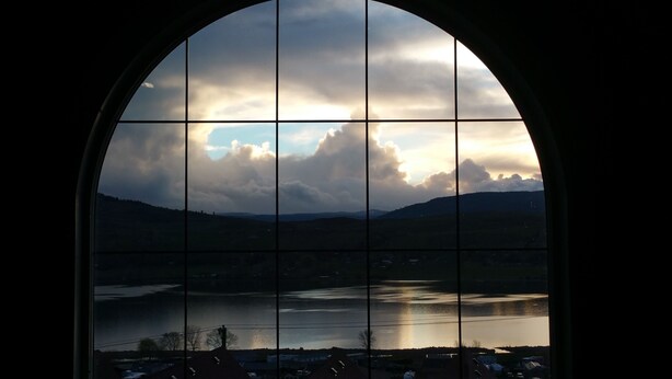 A view through a window with a grid pattern, overlooking a body of water and distant hills. - The Castle at Swan Lake (Vernon)