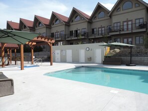 A swimming pool with a pergola and lounge chairs, surrounded by a building with multiple balconies and a clock on the wall. - The Castle at Swan Lake (Vernon)