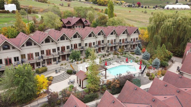 Un hotel de varios pisos con zona de piscina, rodeado de árboles y un paisaje montañoso.