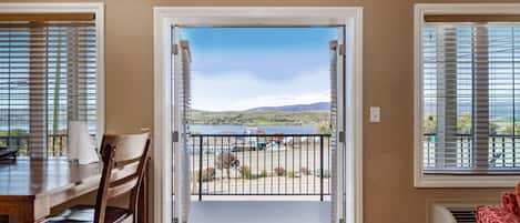 Puerta abierta que da a un balcón con vistas a un lago y colinas al fondo.