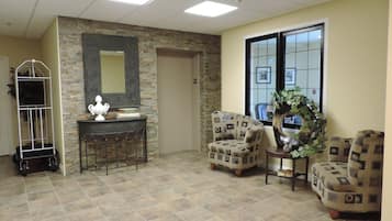 A lobby with a stone wall, a mirror, two patterned armchairs, a small table with a vase, and a plant.