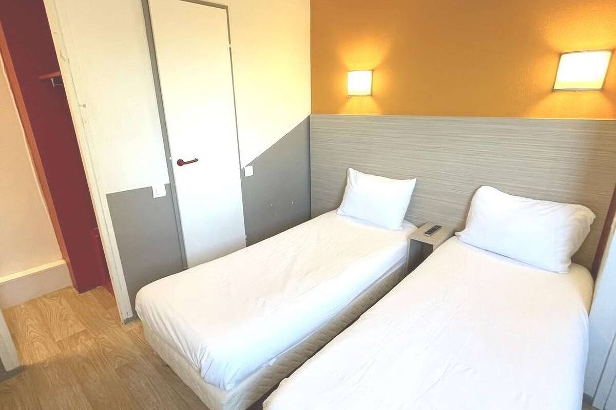 A hotel room with two single beds, a wooden floor, a door, and two wall-mounted lights.