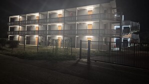 Een meerlaags gebouw met balkons, een hekwerk en een goed verlichte gevel.