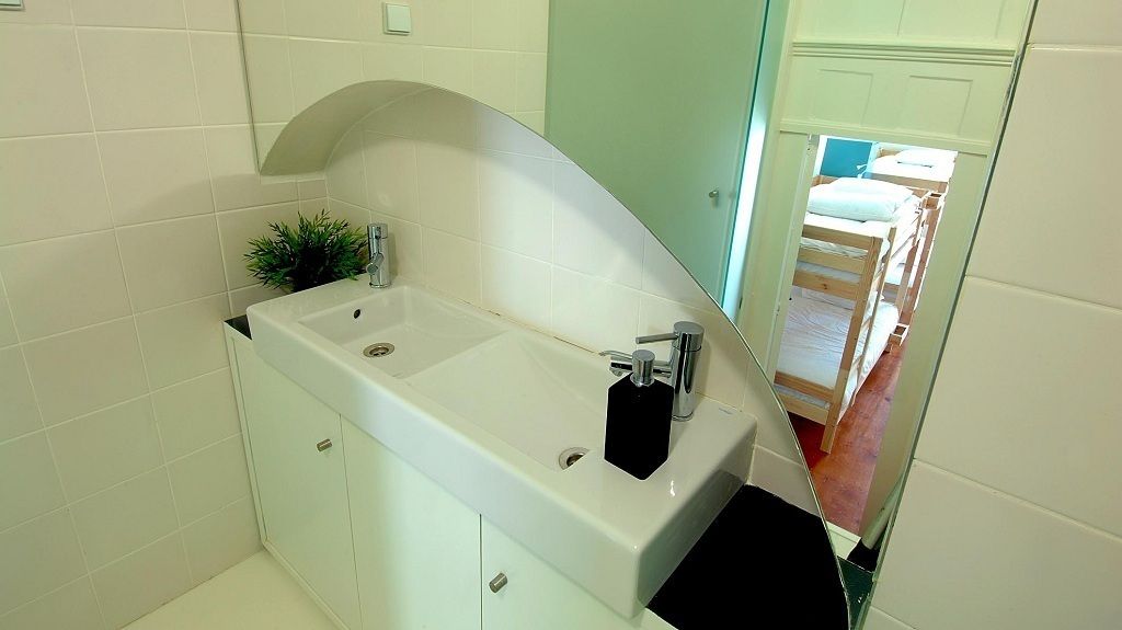 Un baño con lavamanos blanco, un espejo y una pequeña planta.