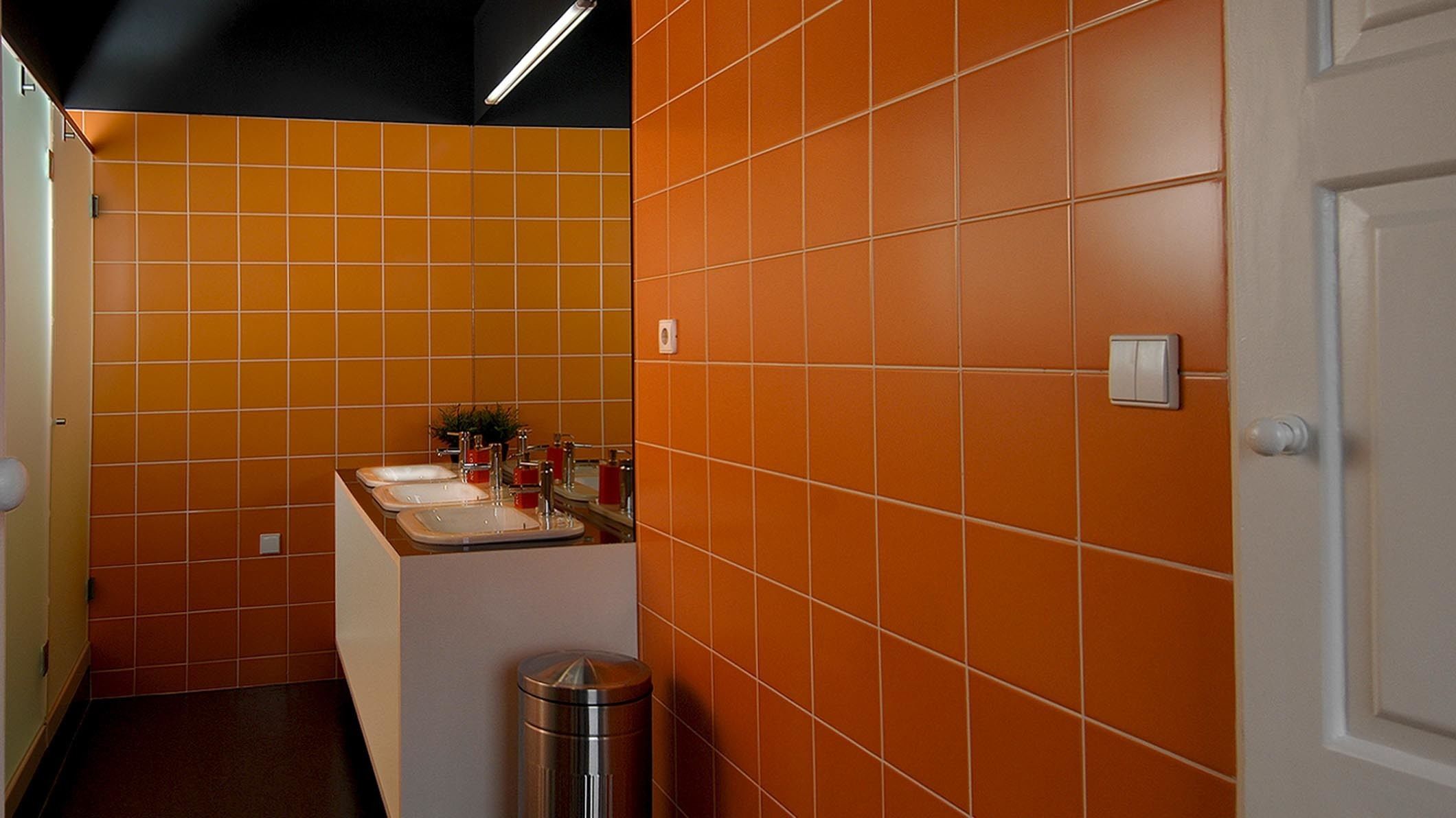 A bathroom with orange tiles, a sink, a mirror, and a trash can.