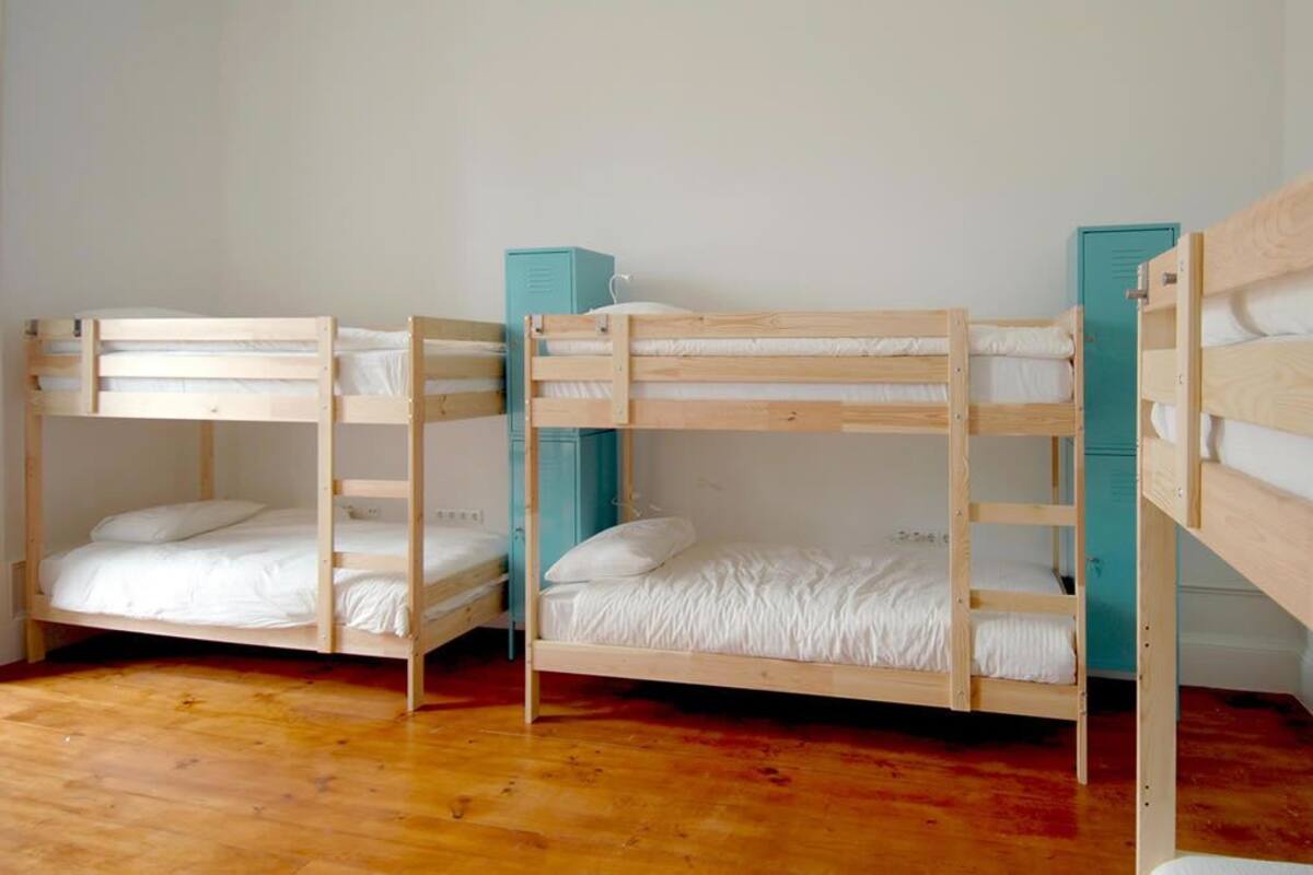 Una habitación con tres literas, suelo de madera y taquillas azul verdosas.