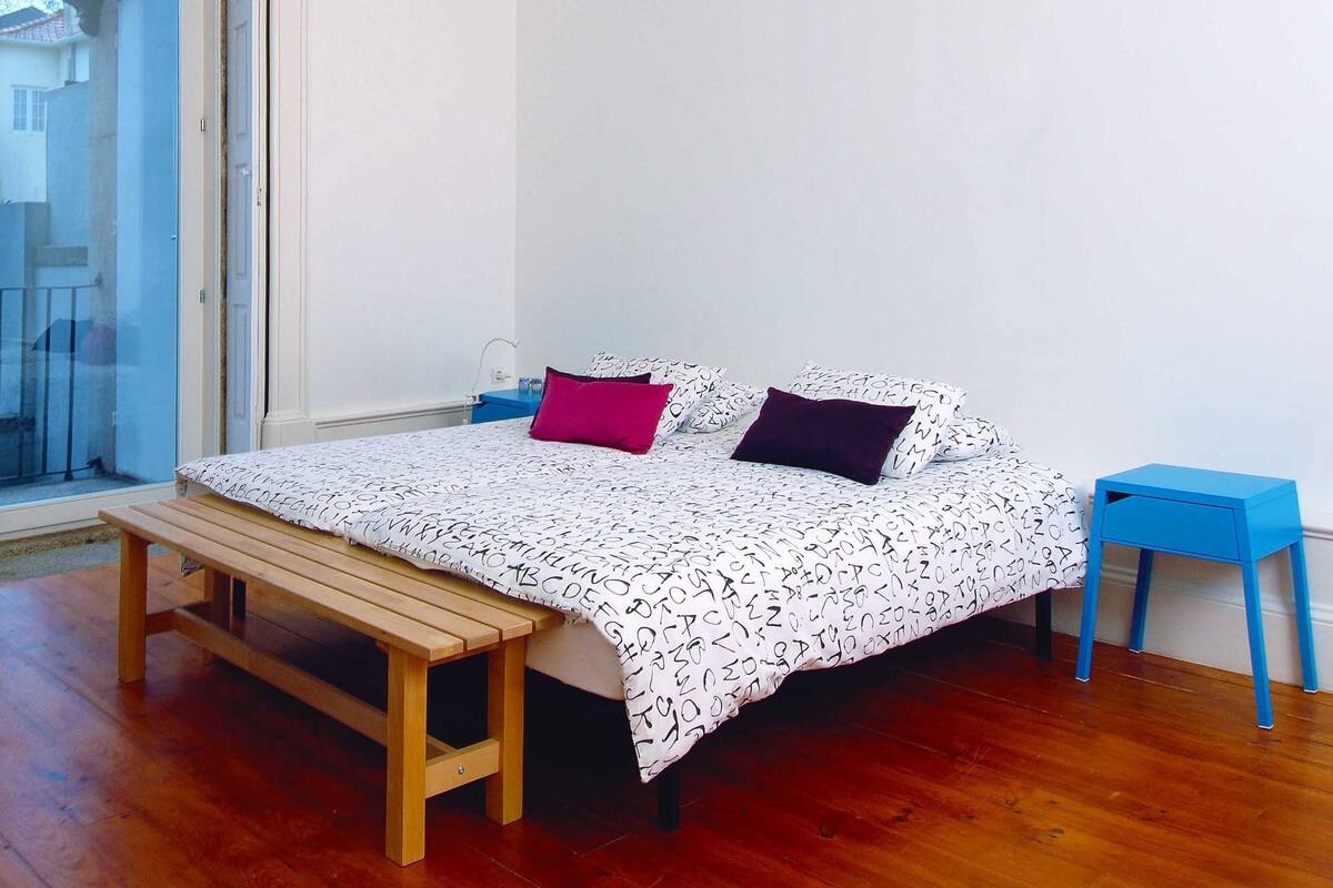 Un dormitorio con cama, una banca, una mesita de noche y una ventana.