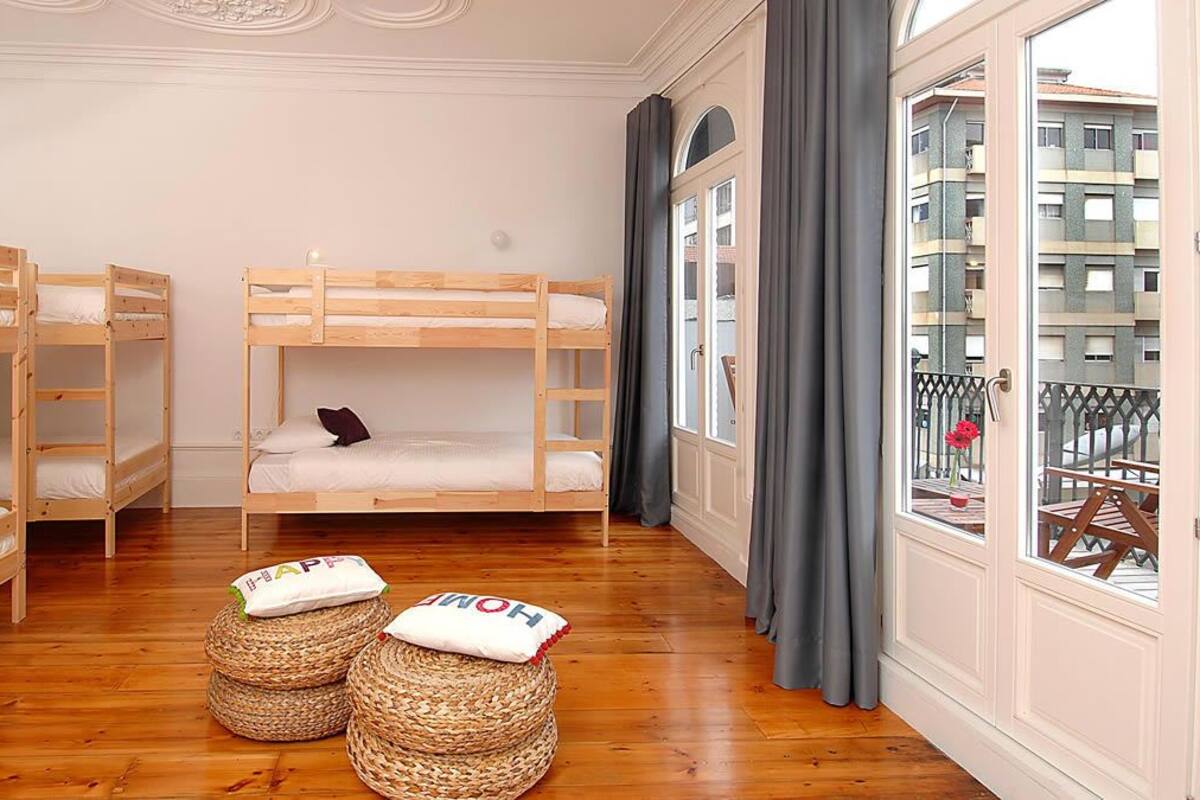 Una habitación con tres literas, un balcón con vistas a edificios y una ventana con cortinas.