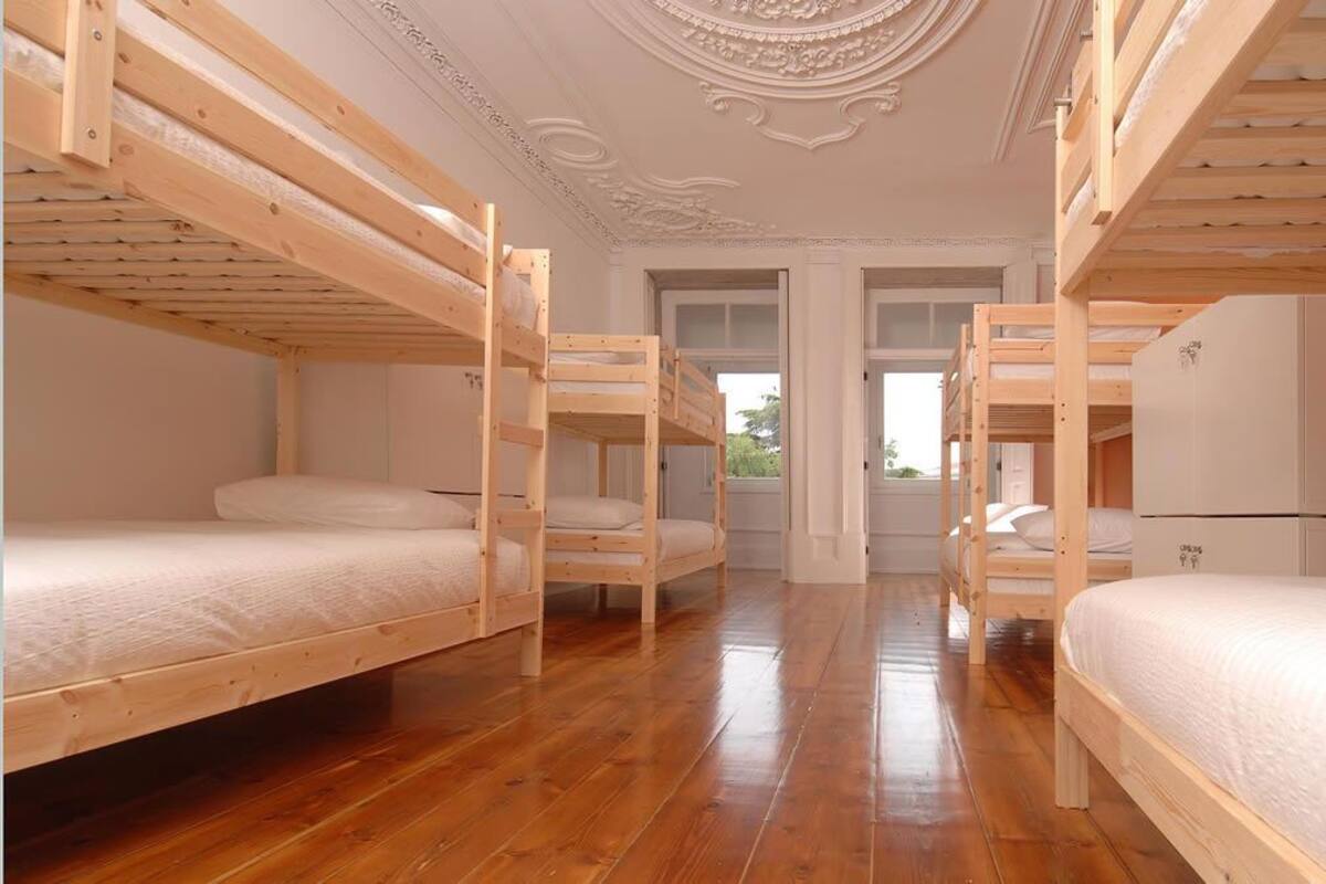 Una habitación con cuatro literas, suelo de madera, techo blanco con molduras ornamentales y un refrigerador blanco.