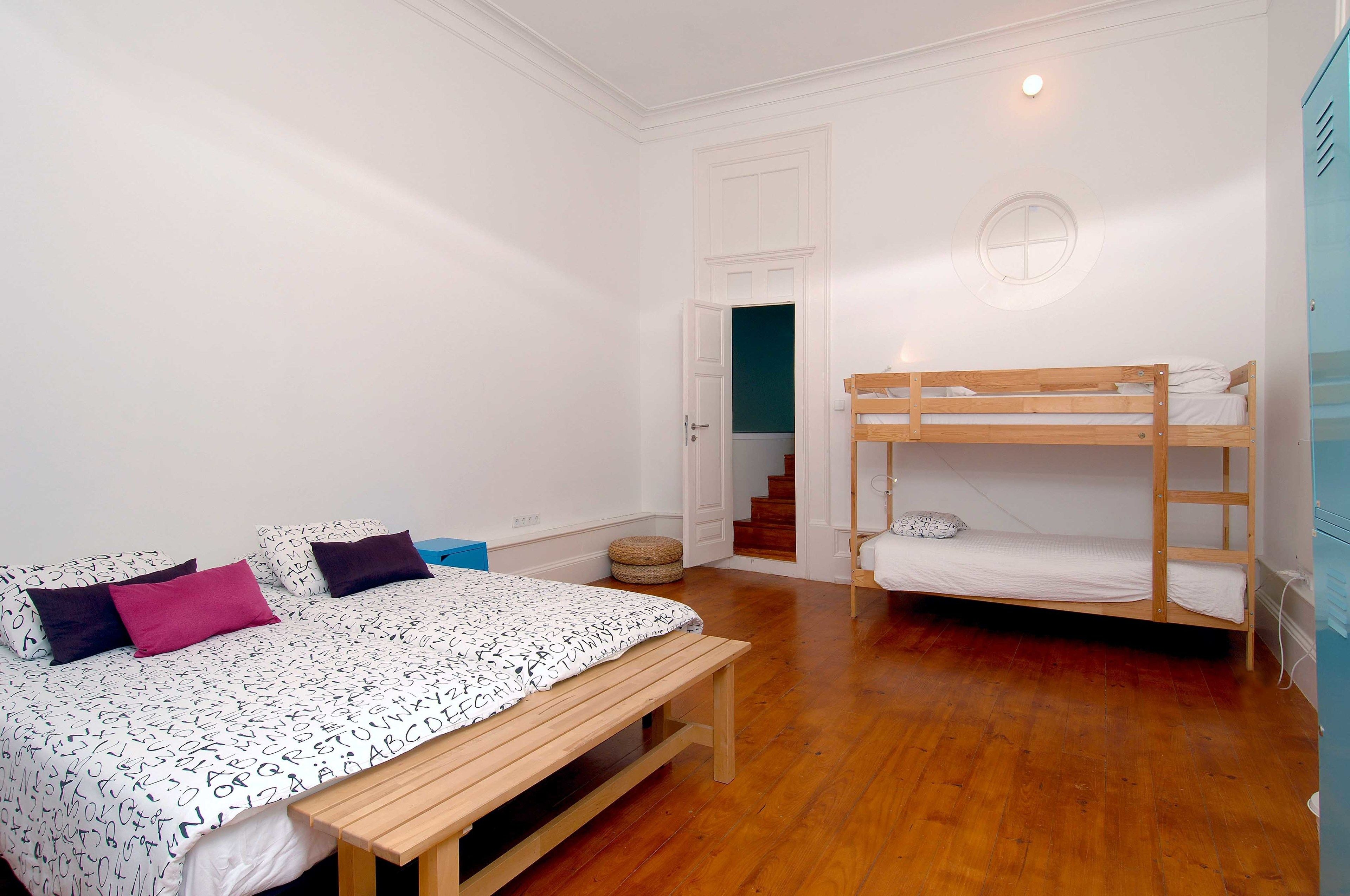 Een slaapkamer met een stapelbed, een enkel bed, een houten bankje en een trap naar een verdieping boven.