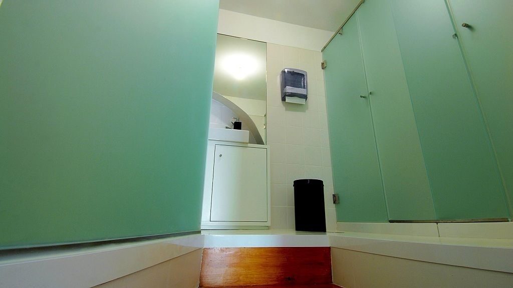 Un couloir étroit aux murs verts, une porte blanche et un petit coin lavabo avec un miroir.