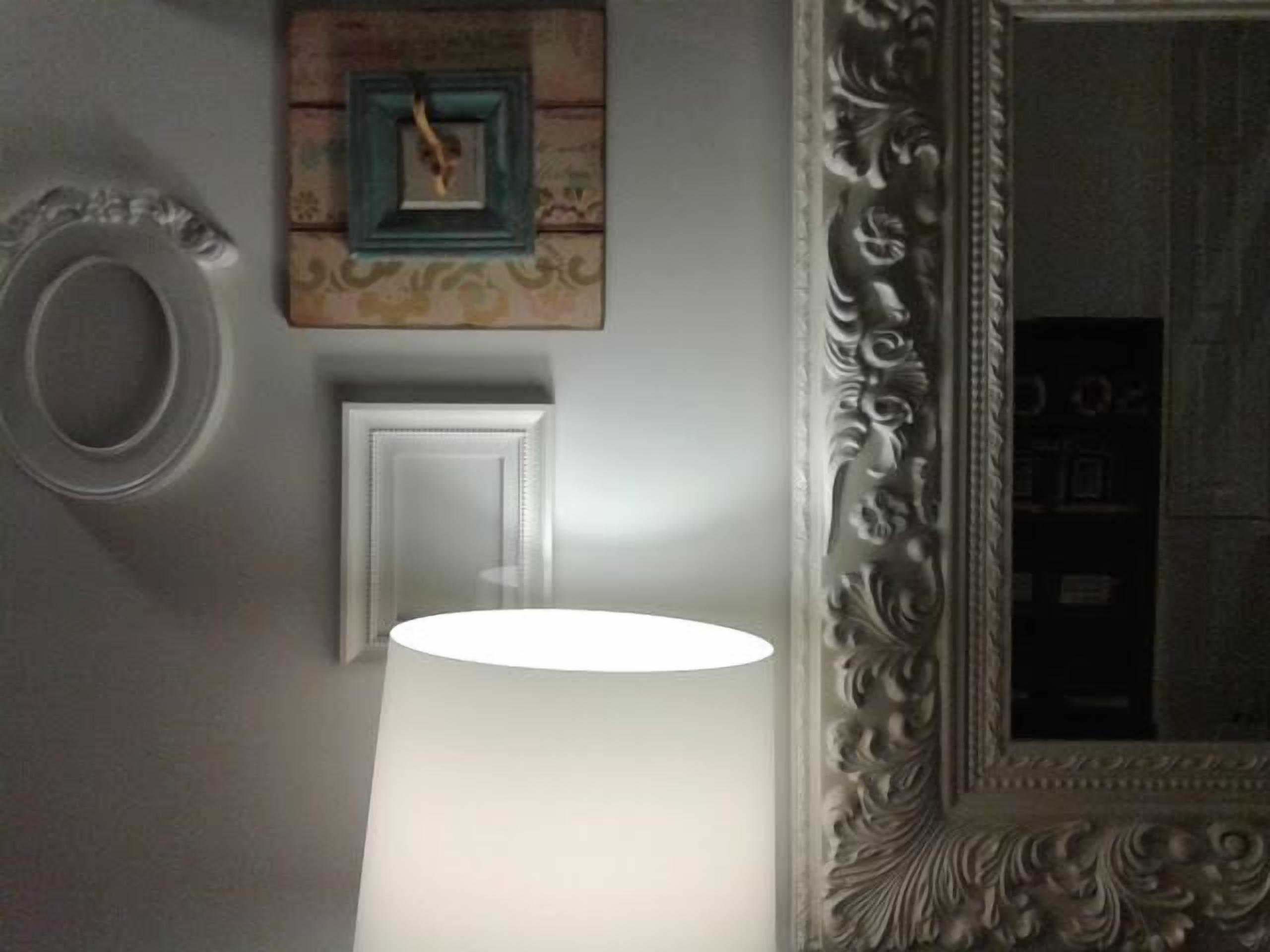 Una habitación con un espejo grande, una puerta blanca y una lámpara fijada a la pared.