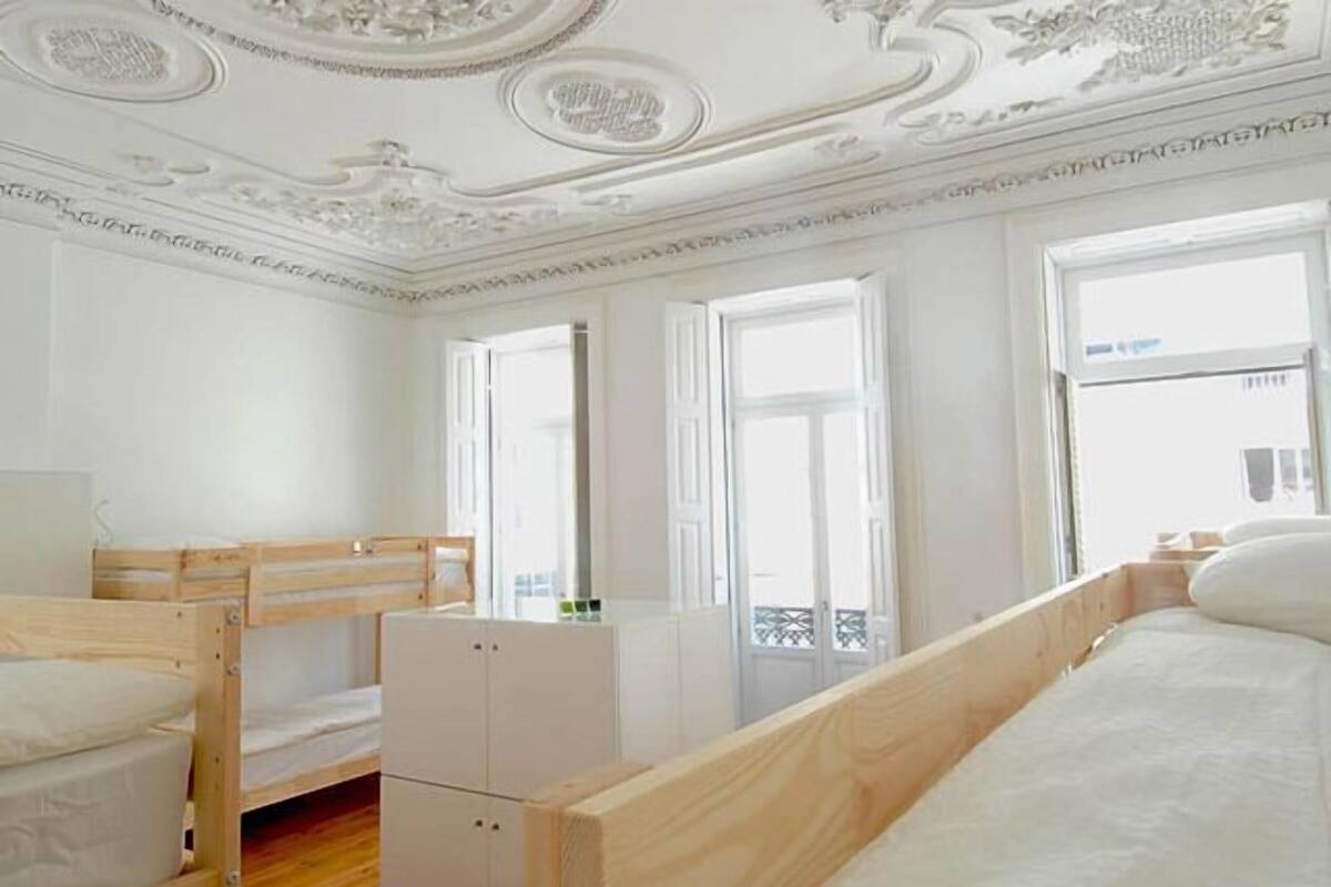 Una habitación con literas, un mueble blanco pequeño y ventanas grandes.