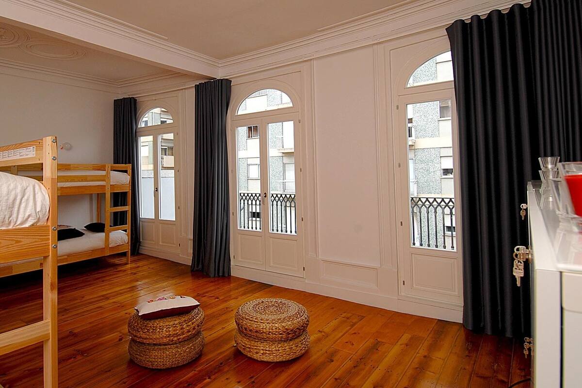 Una habitación con una cama litera, dos cestos de mimbre, un armario blanco y un balcón con barandilla.