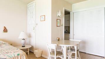 A bedroom with a bed, a bedside table with a lamp, a small table with chairs, a closet, and a door leading to another room.