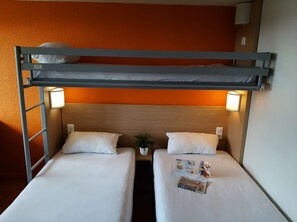 Habitación con literas, dos camas, cada una con una almohada y una lámpara de noche. Hay una pequeña planta en maceta entre las camas y una revista sobre la cama inferior.