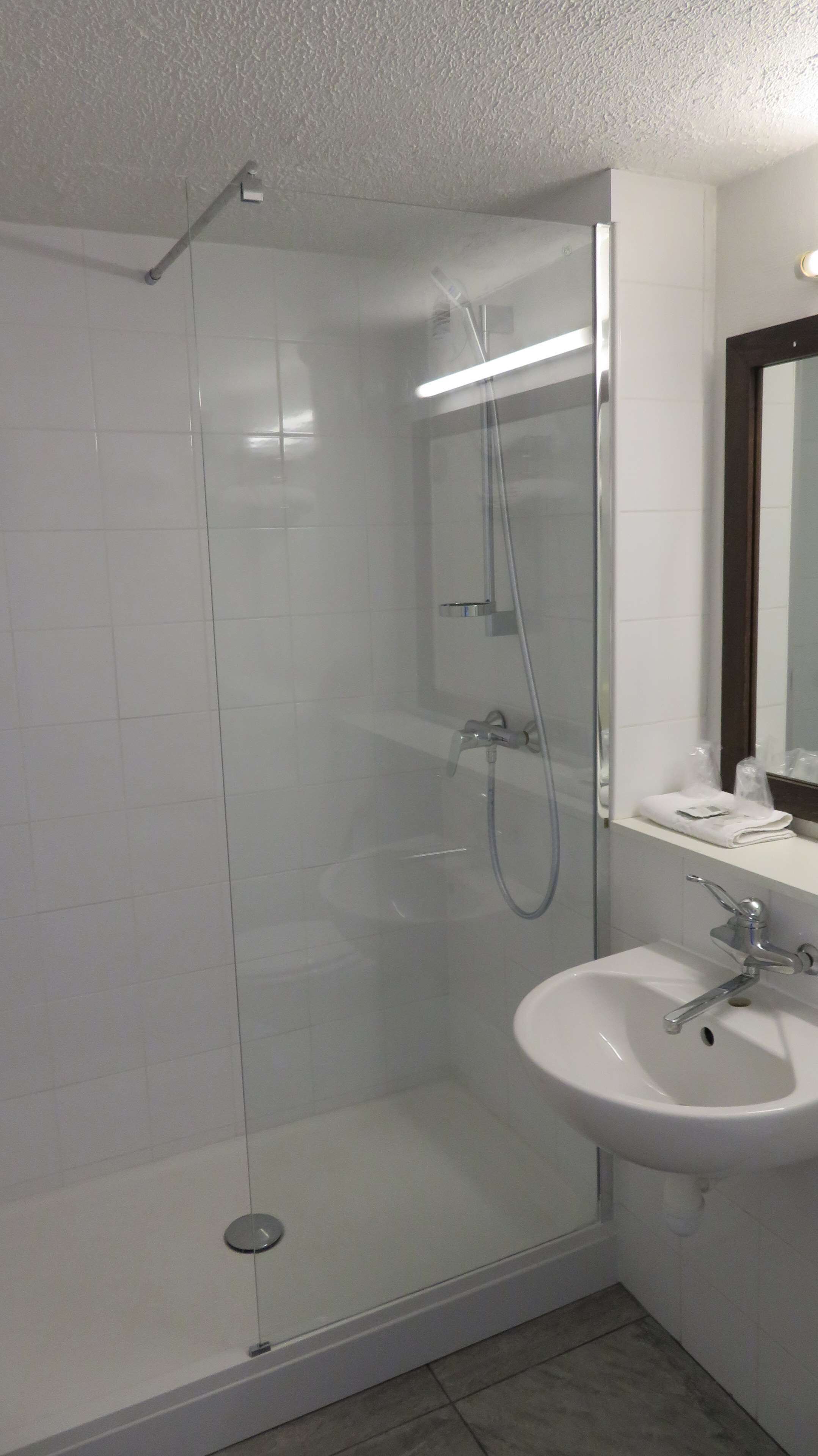 Un baño moderno con ducha envuelta en vidrio, un lavabo blanco y un espejo.