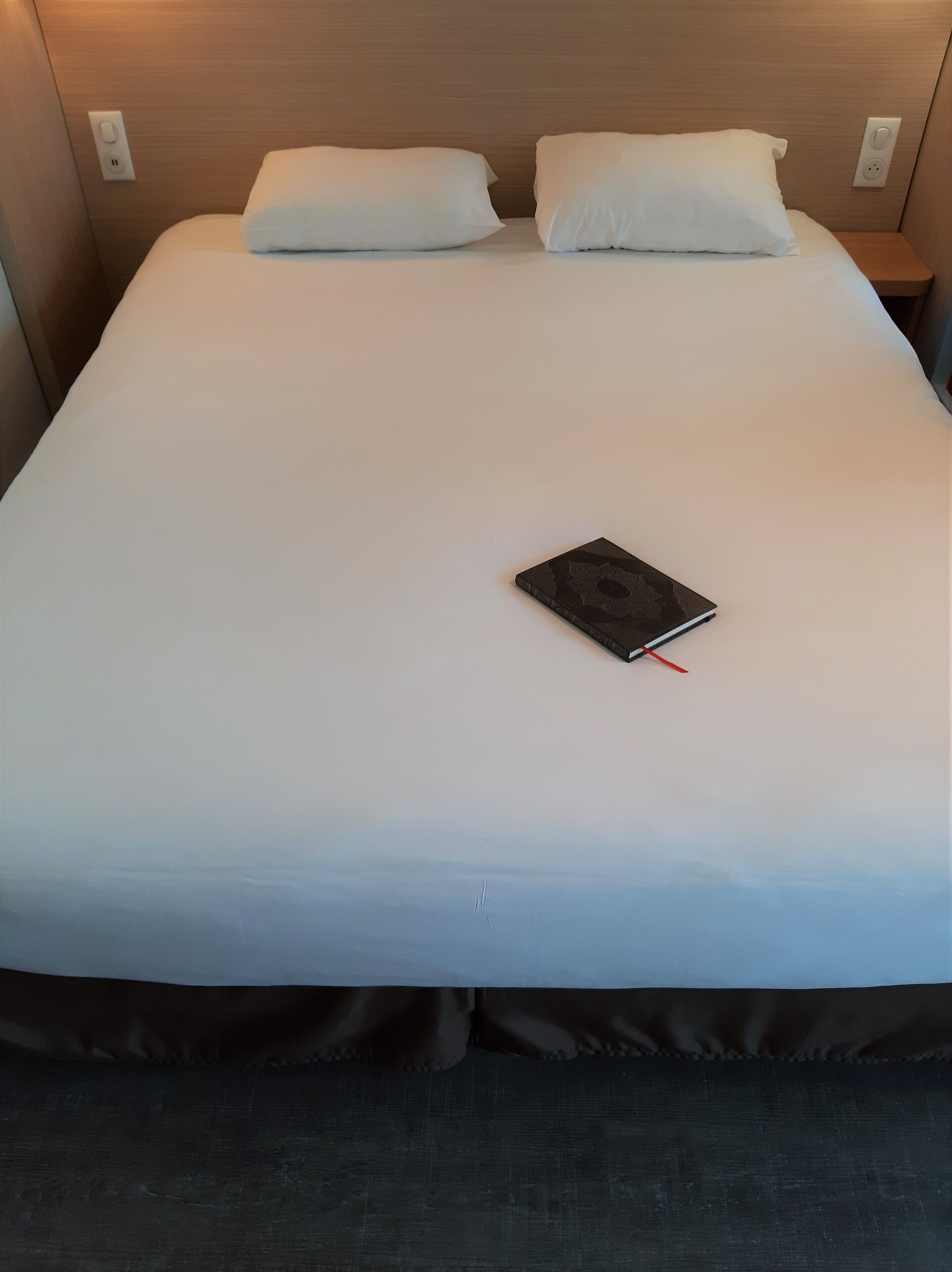 Una cama bien hecha con sábanas blancas, un libro negro y un lazo rojo.