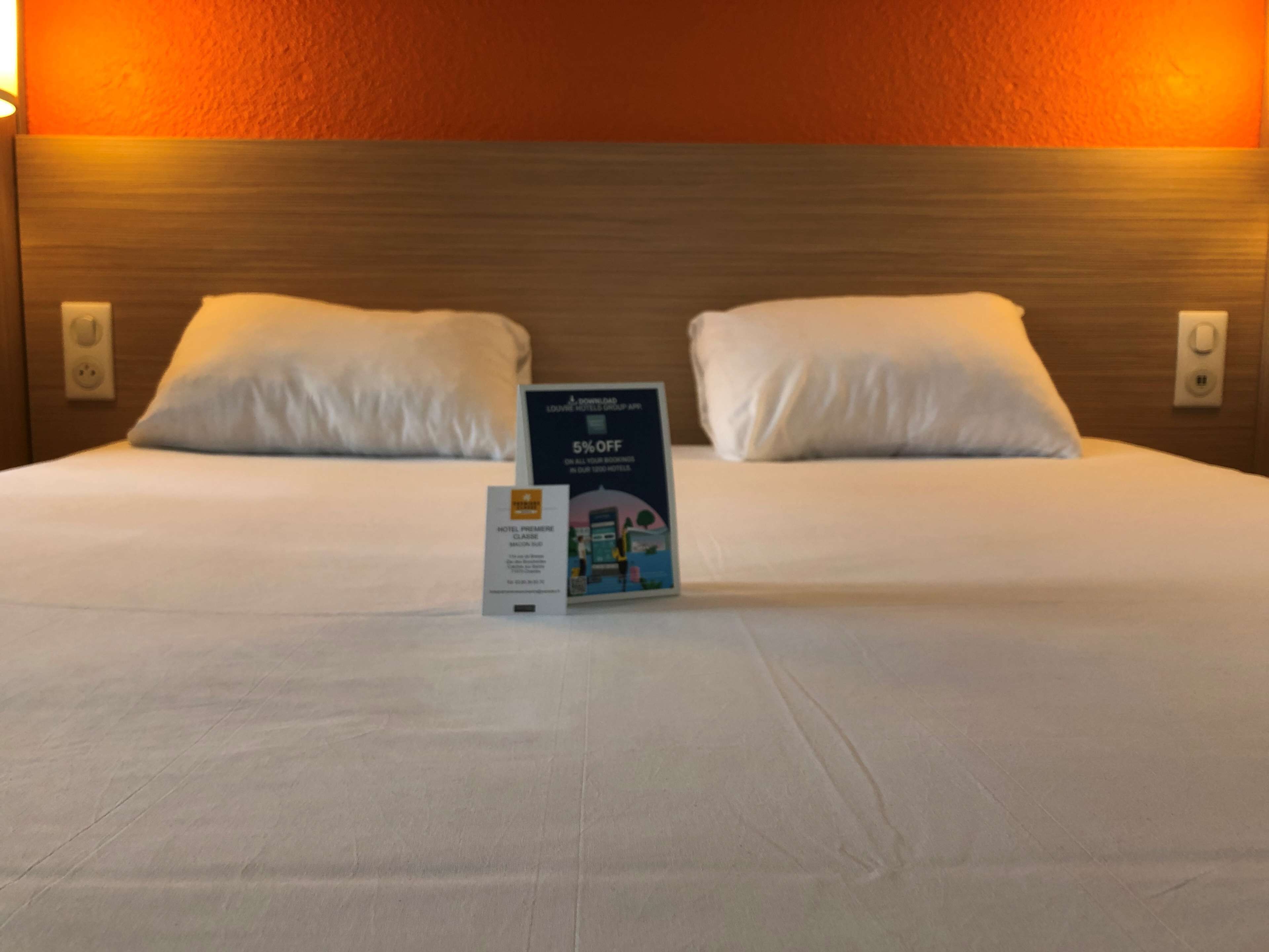 A neatly made bed with white linens and pillows, a sign on the bed, and a wooden headboard.