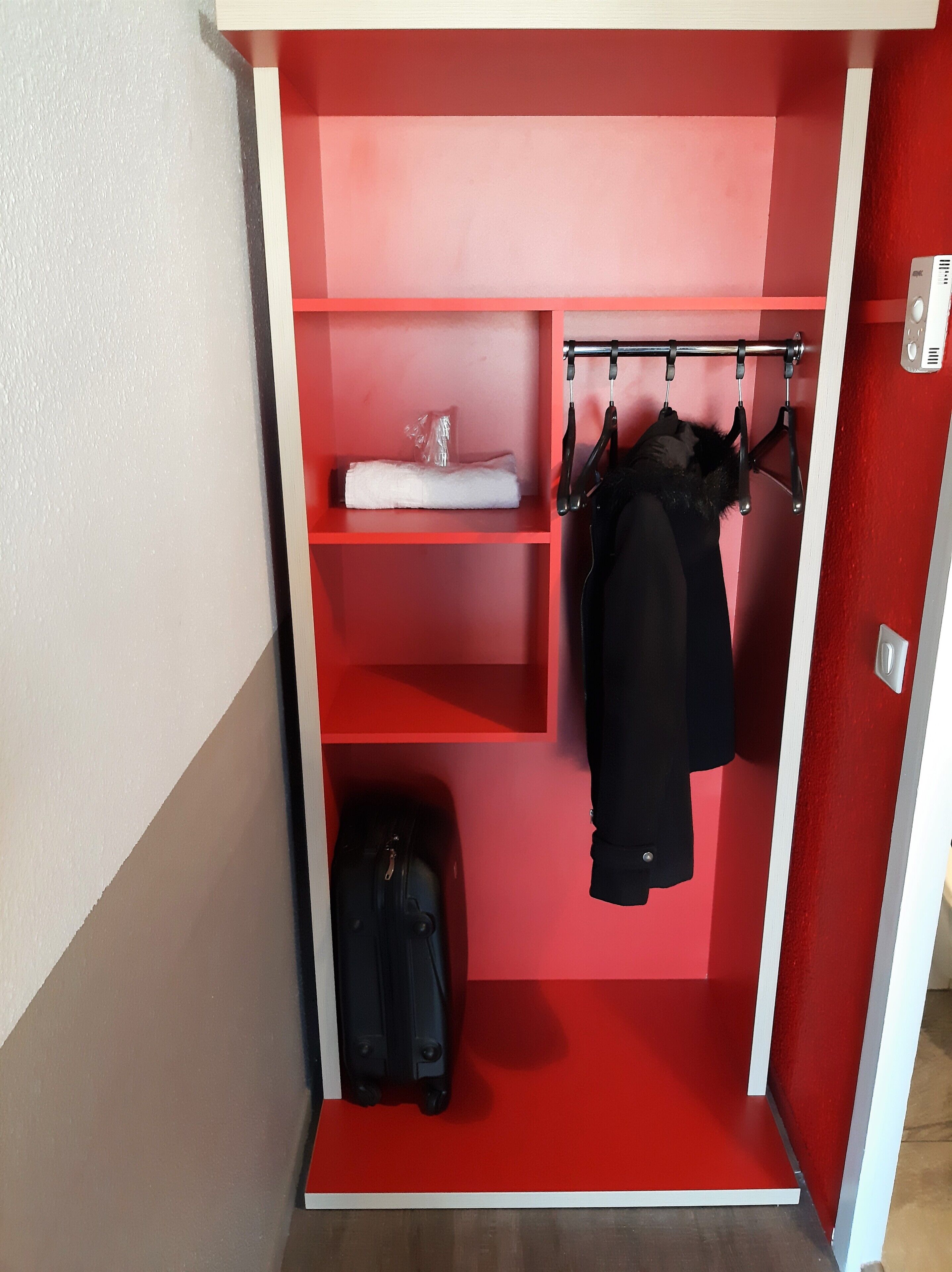 A red and white closet with shelves, a hanging rod, and a suitcase.