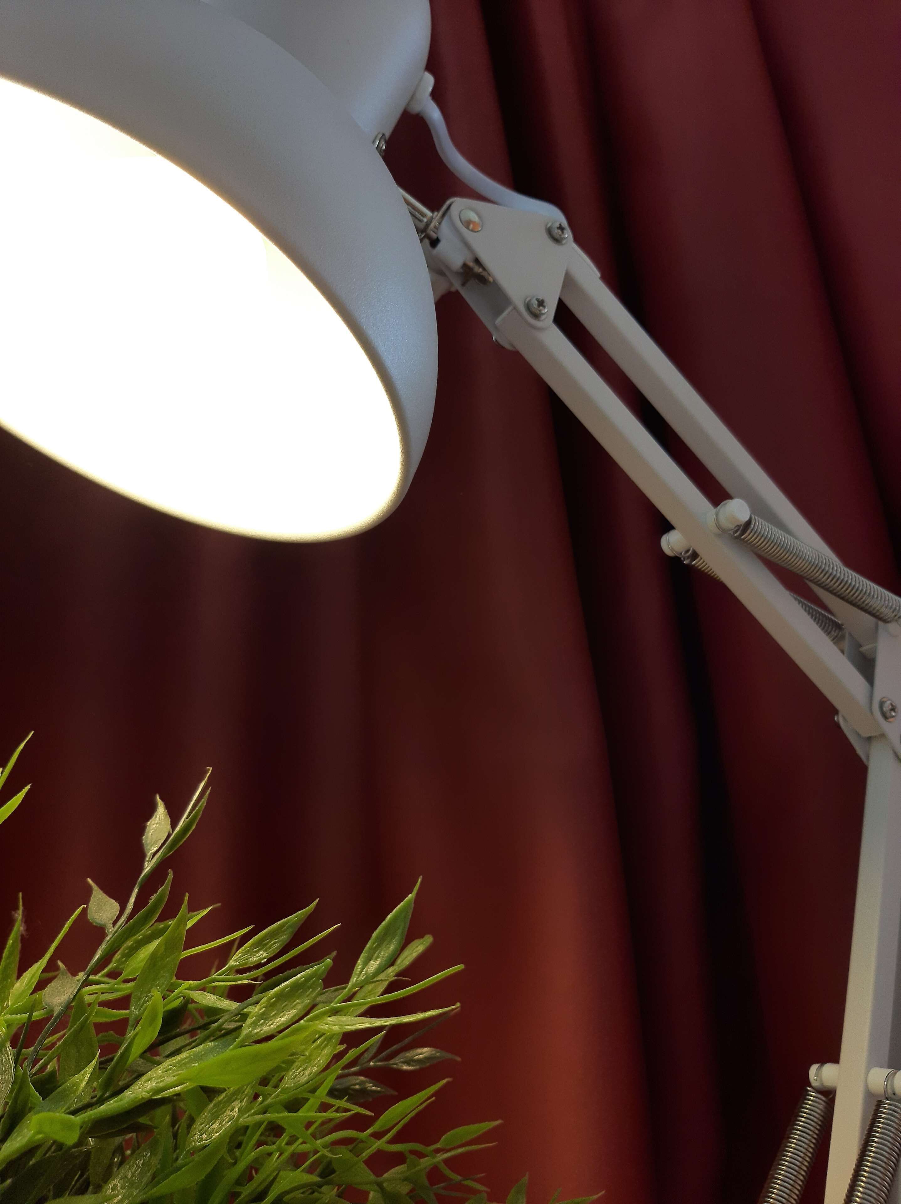 Une lampe de bureau blanche, dotée d’un bras flexible, placée devant un rideau rouge.