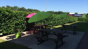 A picnic area with tables and green umbrellas, surrounded by well-maintained hedges. - Premiere Classe Mâcon Sud (Chaintre)