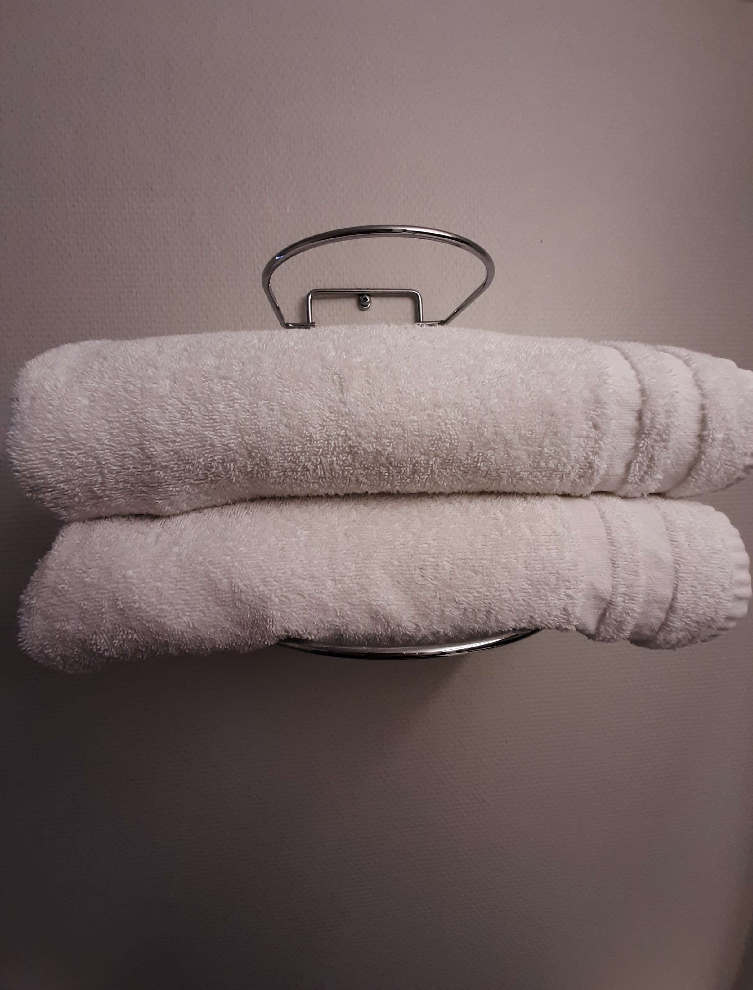 Twee witte handdoeken gevouwen en opgehangen aan een metalen handdoekhouder voor een effen muur.