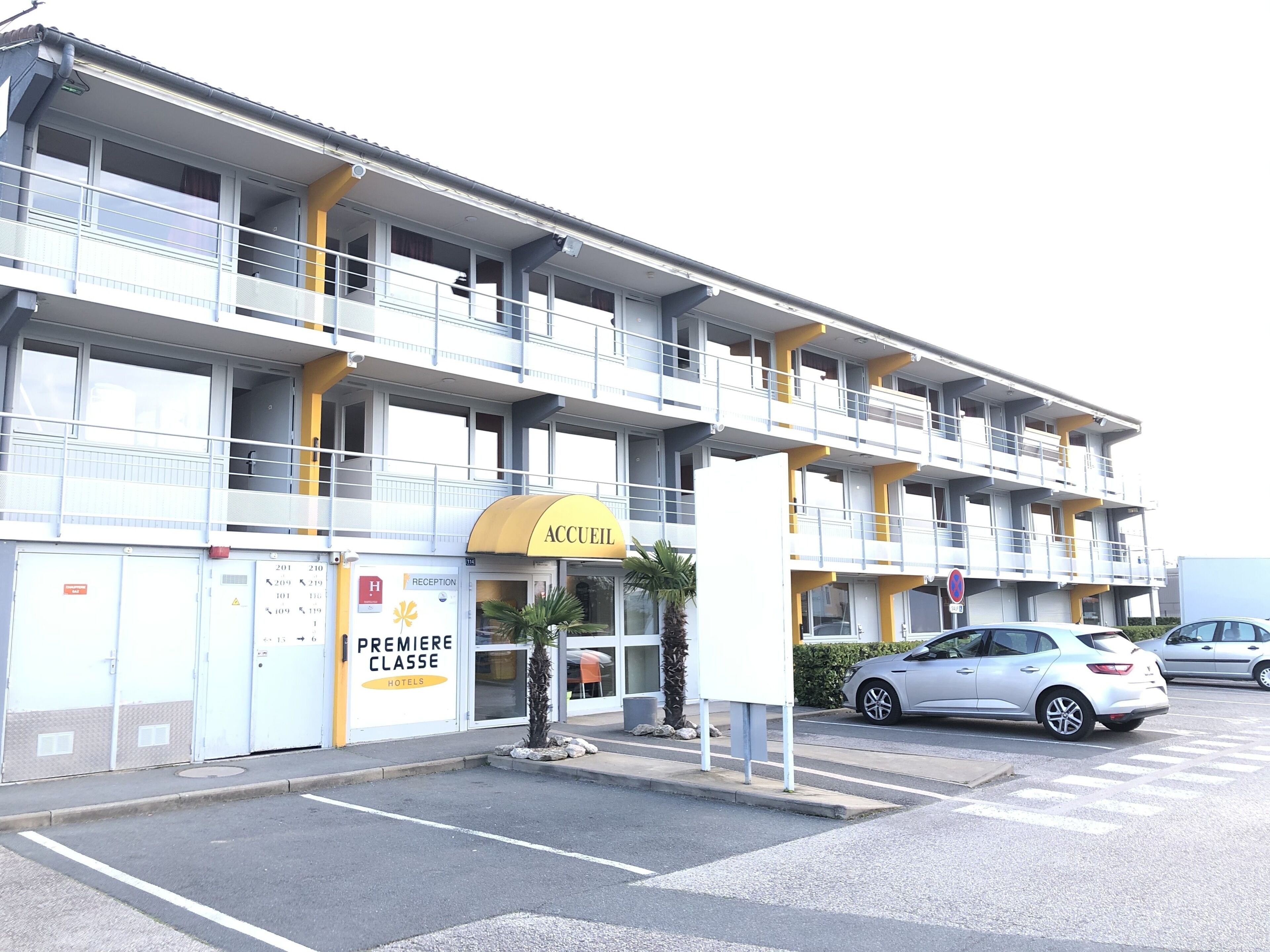 A multi-story hotel with a reception area, a parking lot, and a building with balconies.