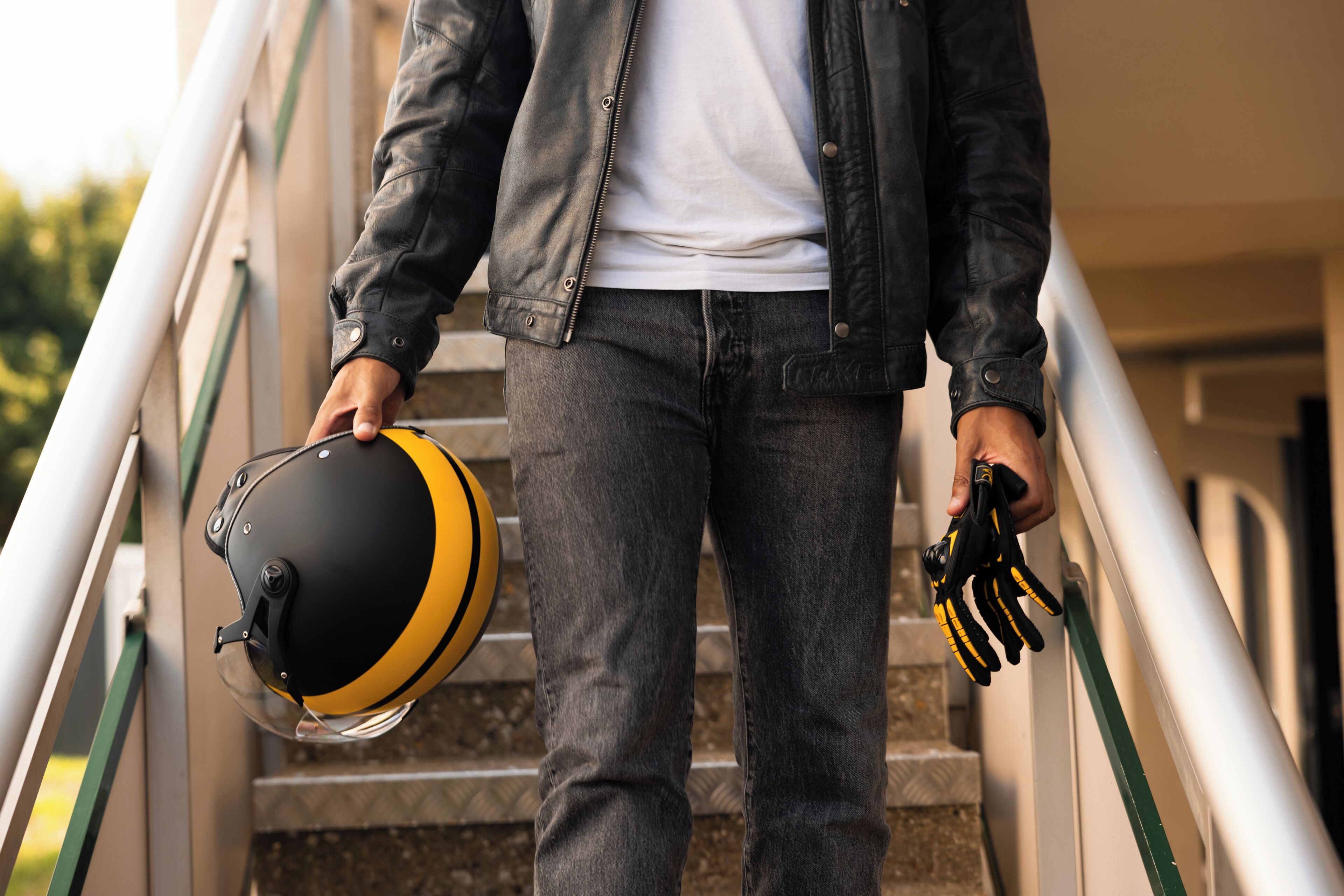 A person descending a staircase, holding a helmet and gloves.
