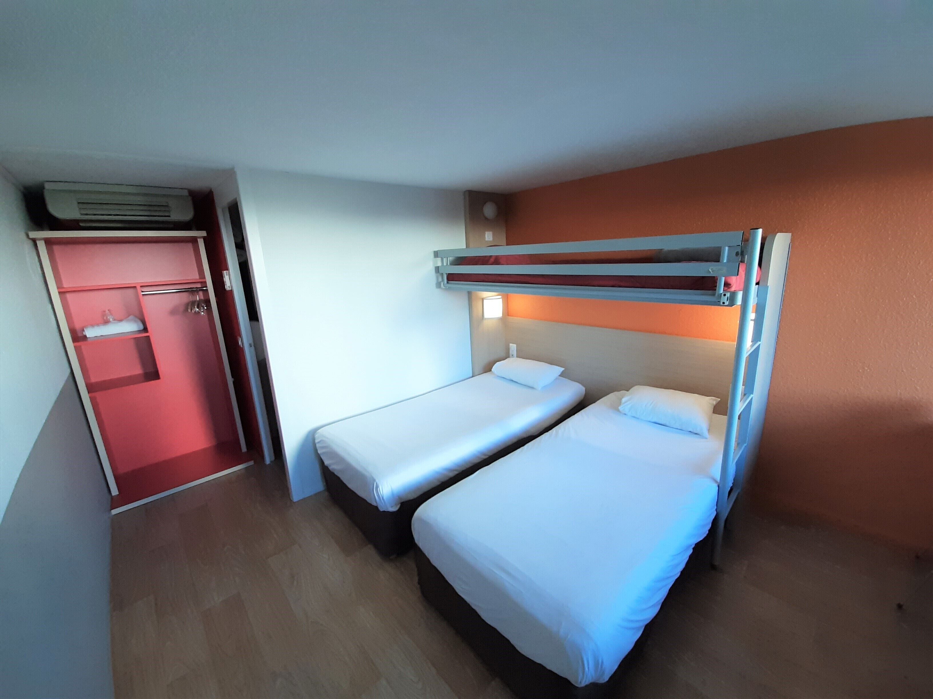 A compact hotel room with two single beds, a red door, and a built-in wardrobe.