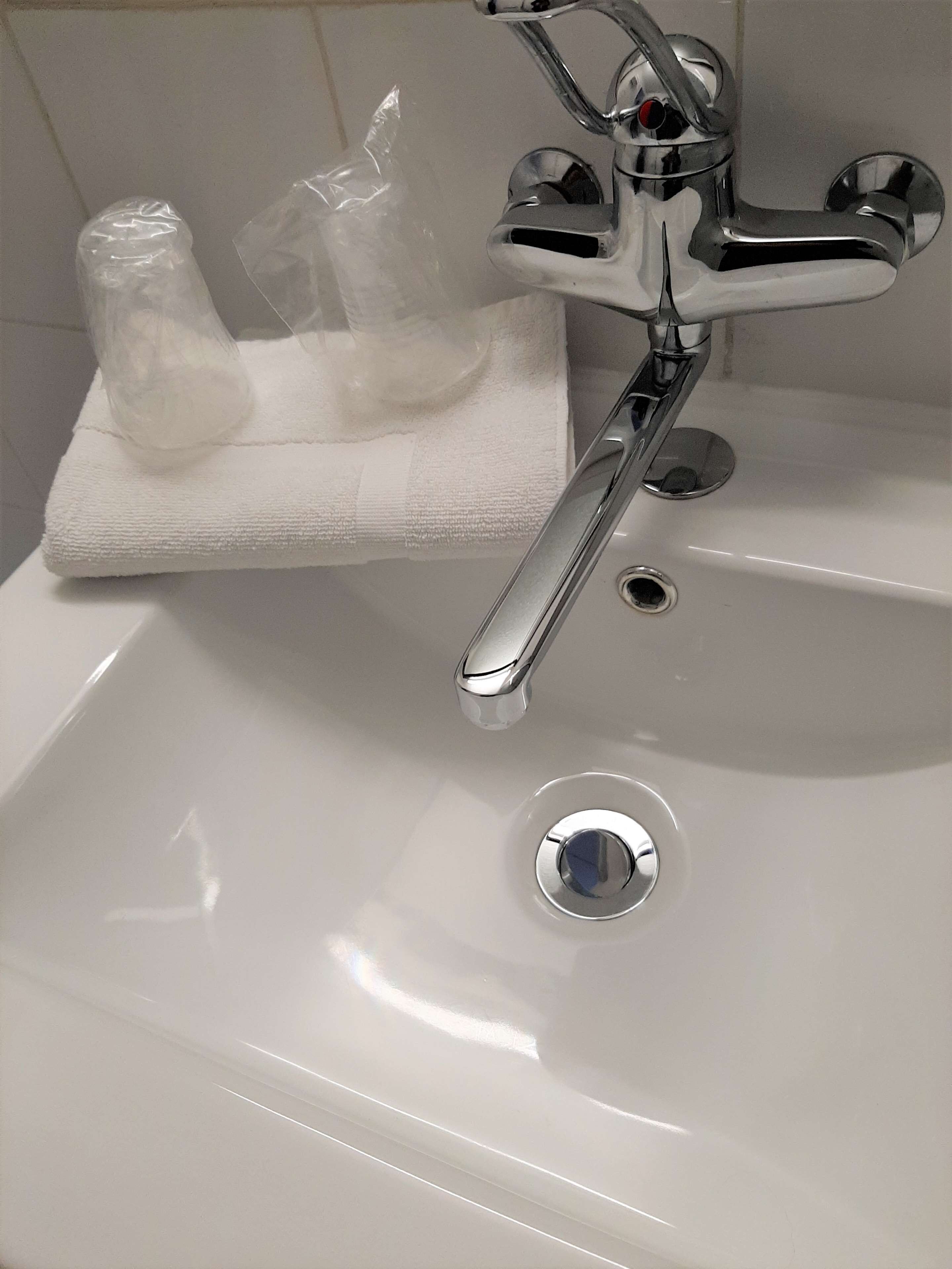 Een badkamermeubel met een wastafel, een chromen kraan, een handdoek en een plastic zak.