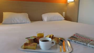 A neatly made bed with white bedding, a tray with breakfast items including croissants, a cup of coffee, and a glass of orange juice, and a newspaper on the side.