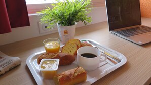 A breakfast tray with croissants, butter, a cup of coffee, and a glass of orange juice on a wooden table. - Premiere Classe Mâcon Sud (Chaintre)