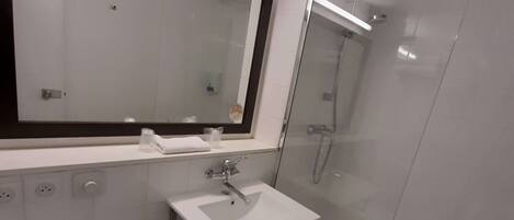 A modern bathroom with a white sink, a large mirror, a toilet, and a glass-enclosed shower.