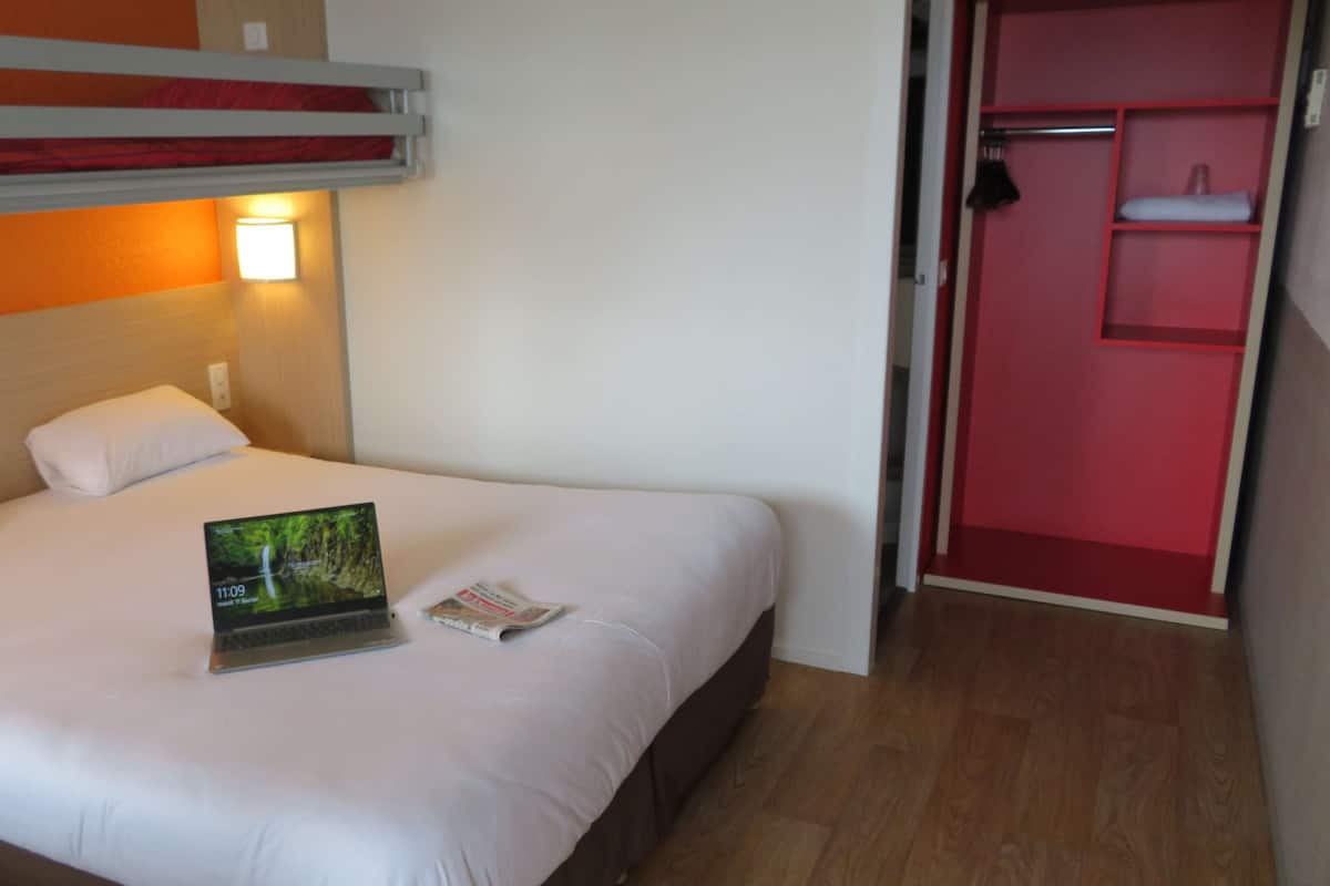 A hotel room with a bed, a laptop, and a magazine on the bed.