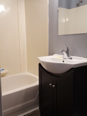 A bathroom with a white bathtub, a sink with a mirror above it, and dark wooden cabinets. - Palace Inn Motel (Sarnia)
