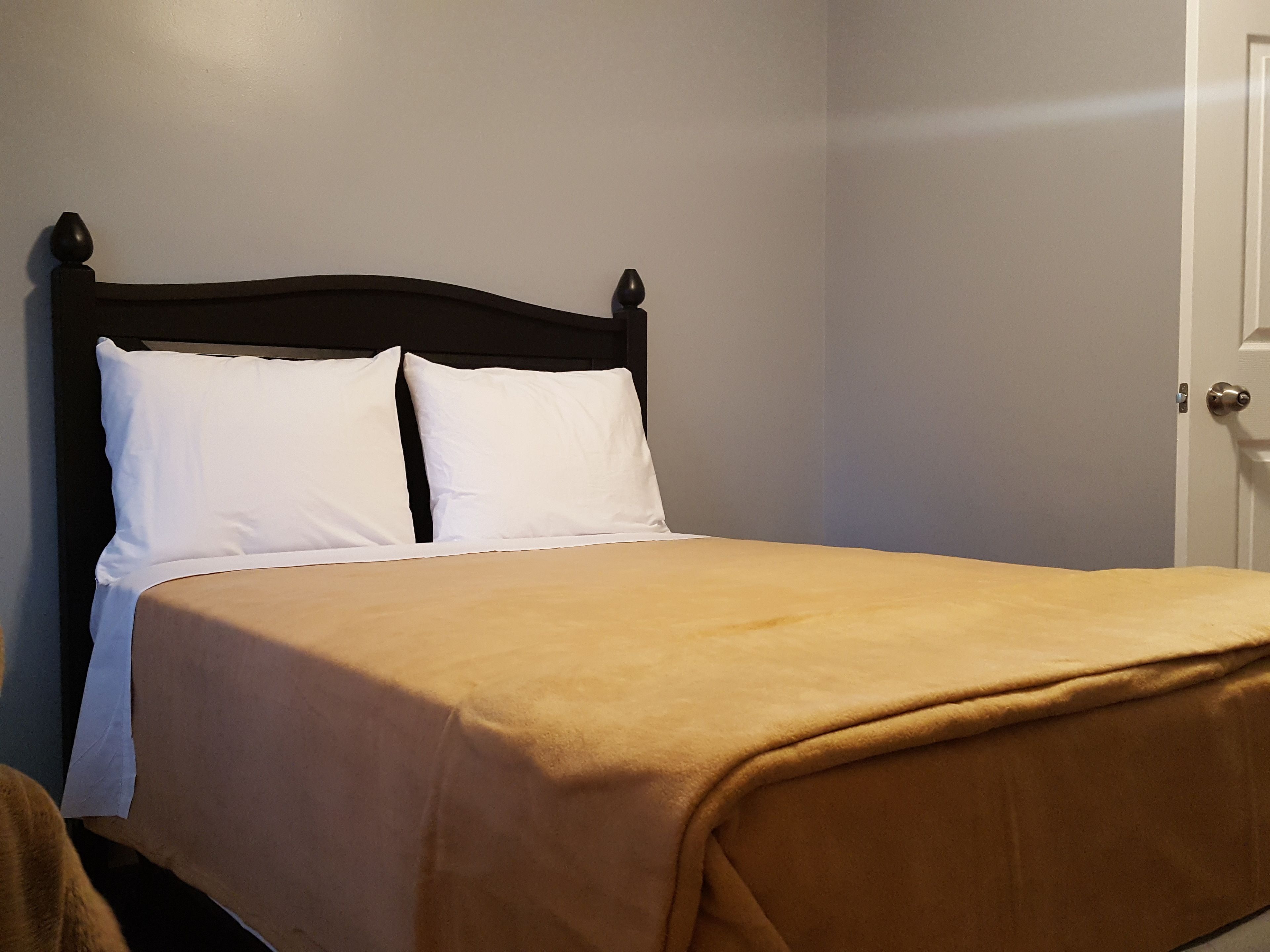 A neatly made bed with a dark headboard and white pillows, set against a plain wall.