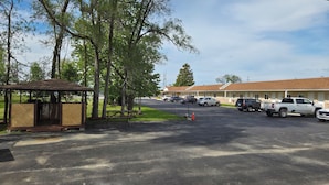 Um motel com estacionamento, um gazebo e um edifício com telhado marrom.