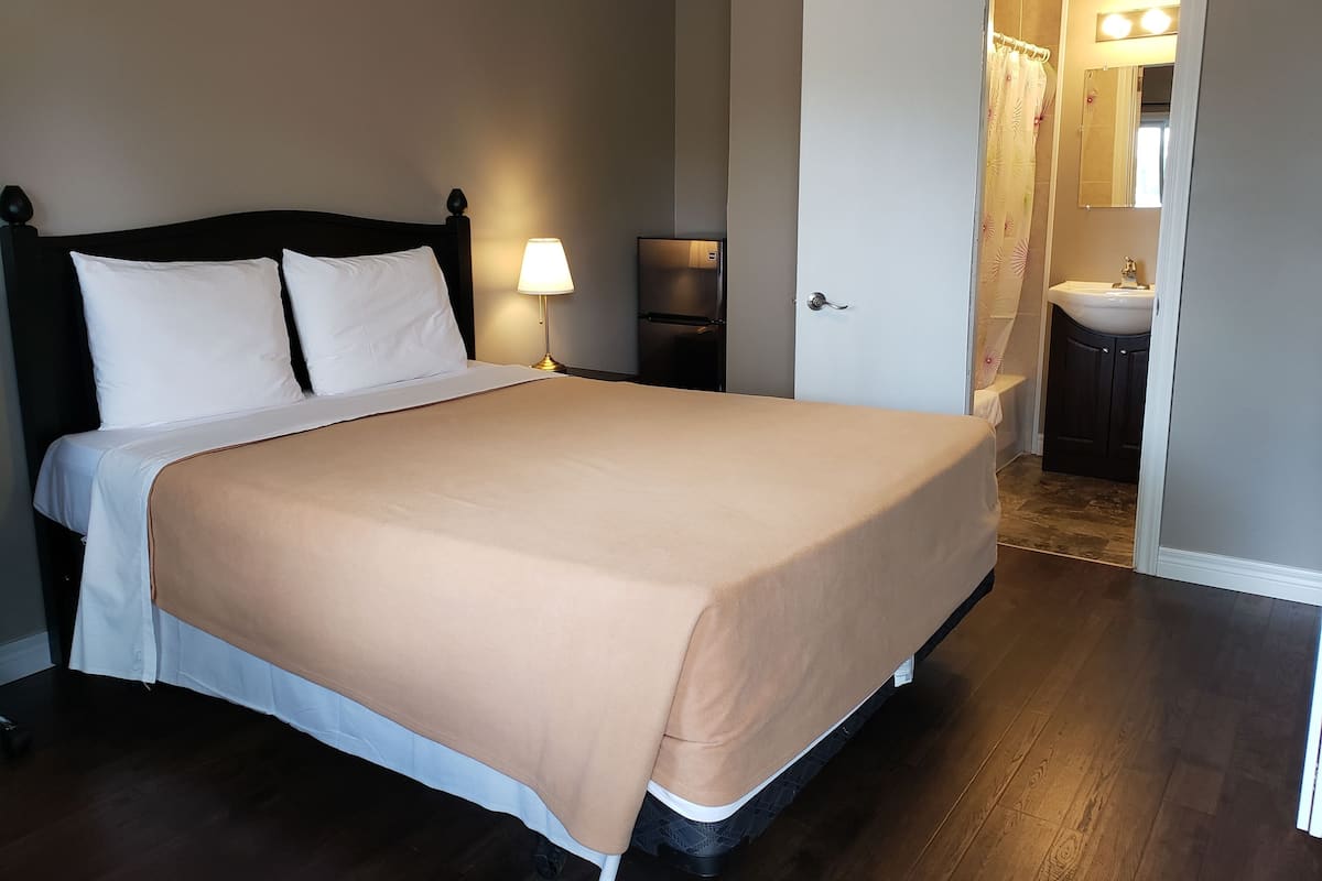 A neatly made bed with a beige bedspread, a bedside lamp, and a dark wooden headboard.