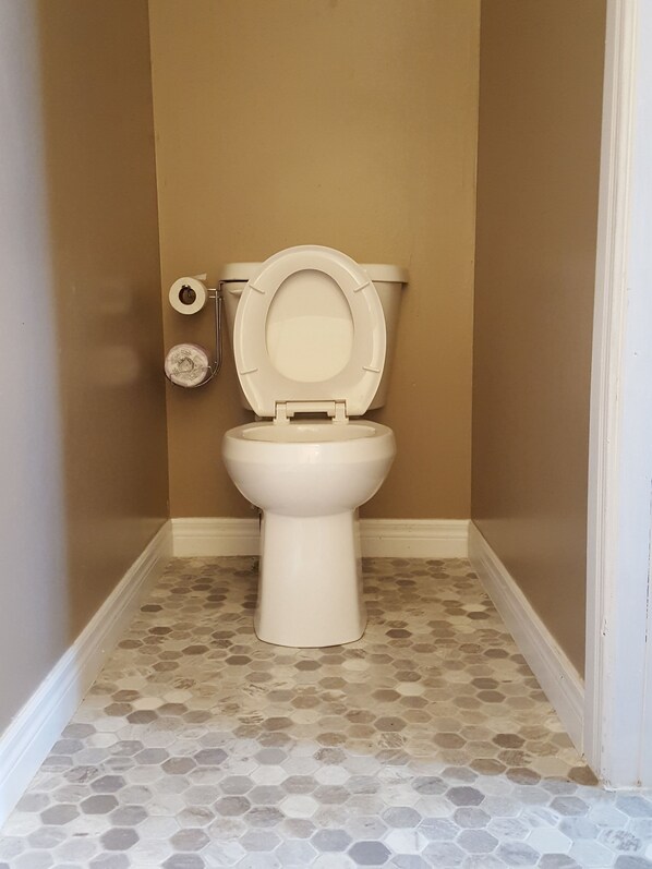 Un baño con inodoro, papel higiénico y suelo de baldosas hexagonales.