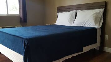 Un lit bien fait, avec une couvre-lit bleue et des oreillers blancs, une tête de lit en bois et une fenêtre avec des rideaux.