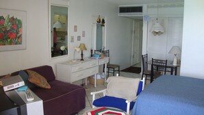 A compact hotel room with a single bed, a small desk with a chair, a sofa, and a dining area with a table and chairs. - Ocean Suite Beach Front at Mobay Club (Montego Bay)