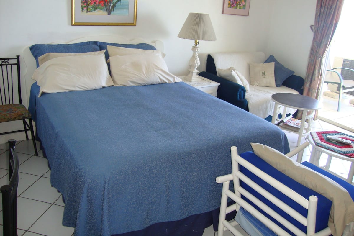 A bedroom with a large bed, a bedside table, a chair, a small table, and two paintings on the wall.