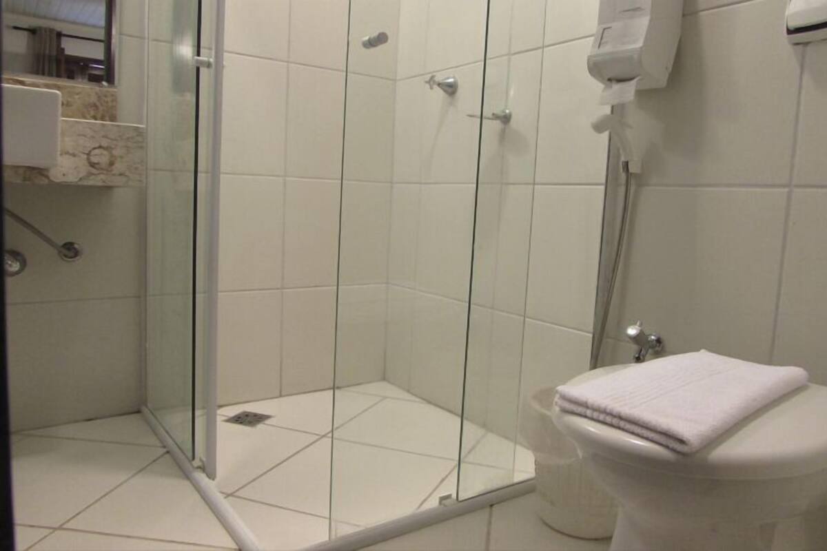 A bathroom with a glass-enclosed shower, a toilet, and a hand dryer.